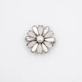 A silver-tone flower-shaped brooch featuring a central white pearl surrounded by clear rhinestones and white enamel petals, set against a plain white background.